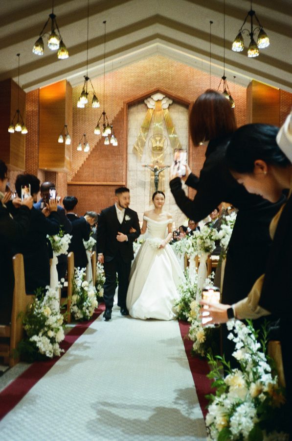 휴대폰을 든 하객들 사이로 버진로드를 걷는 신랑 신부